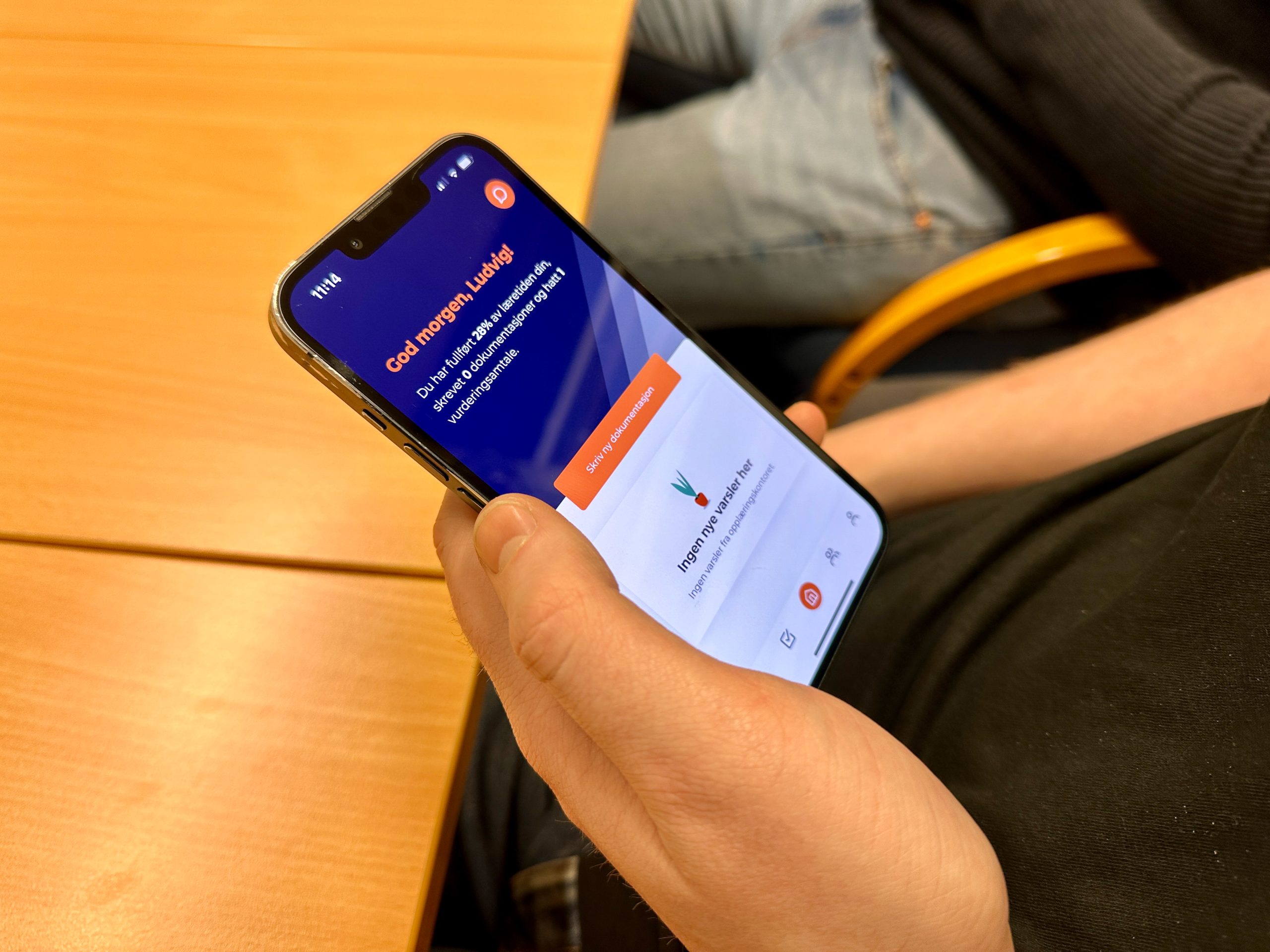 Telefon i hånd med synlig tekst "Hei Ludvig". Bildet viser appen Opplæringskontoret i Dalane bruker i sin oppfølging av lærlinger.
