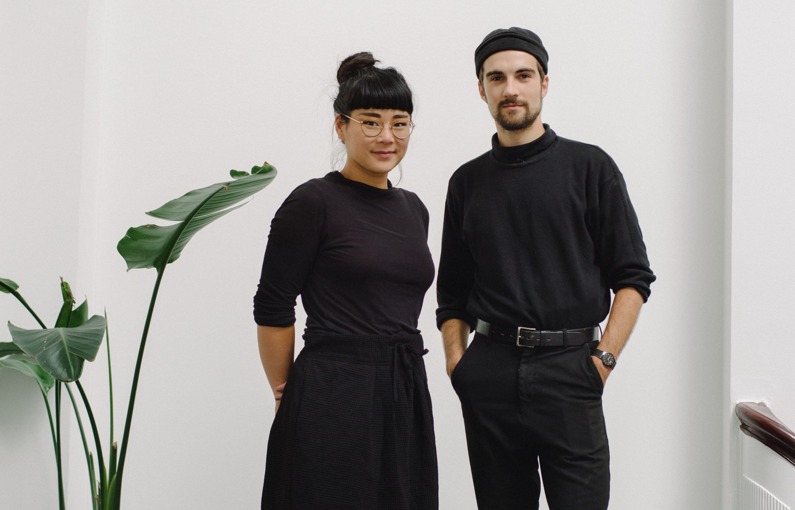 Rhoda Ting og Mikkel Dahlin Bojesen ikledd svarte gensere. Grønn plante til venstre i bildet. Rhoda har på seg briller og Mikkelø en svart lue.