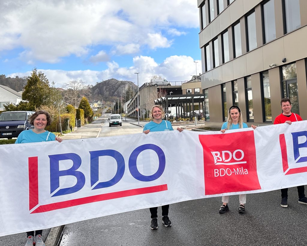 Janne Lædre Vold, Wenche Nodland, Iselin Refsland Kjønnø og Karsten Helleland holder et stor banner med BDO-logo og logo for BDO-mila i Elganeveien. En skimter Egersund forum på høyre side.