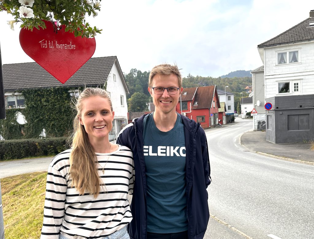 Nora Mathisen Eia i stripete hvit genser, Jonas Glendrange i mørk genser og t-skjorte med påskrift. Over paret henger et hjerte med teksten "tid til hverandre"